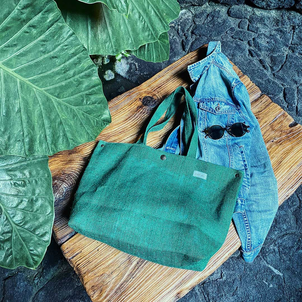 imagen bolso con  complementos, gafas de sol, cazadora tejana, fondo madera y plantas tropicales, evoca la naturaleza y contemporaneidad