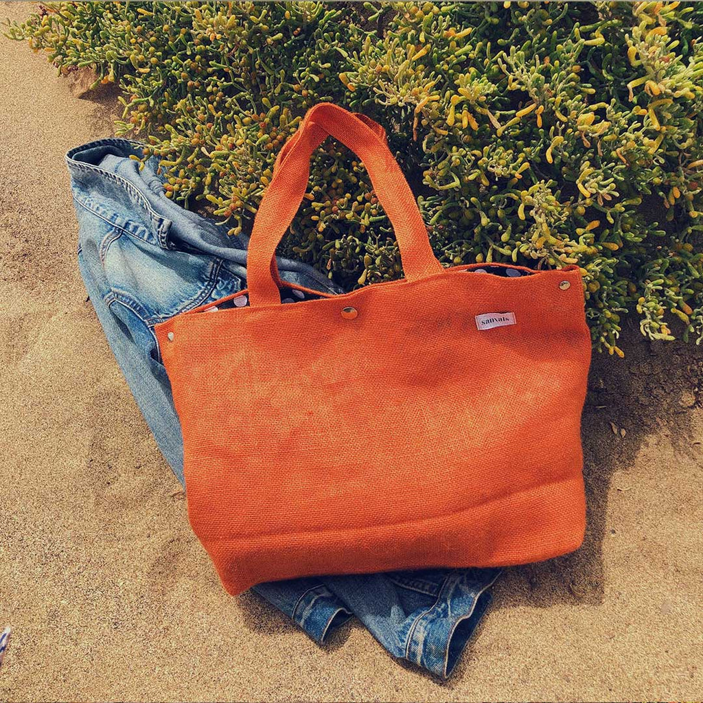 imagen de bolso naranja con cazadora tejana fondo arena playa, imagen moderna, contemporánea